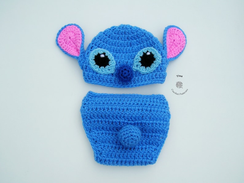 May include: A blue crocheted baby hat and diaper set with pink ears, blue eyes, and a black nose. The set is designed to look like Stitch from the Disney movie Lilo & Stitch.