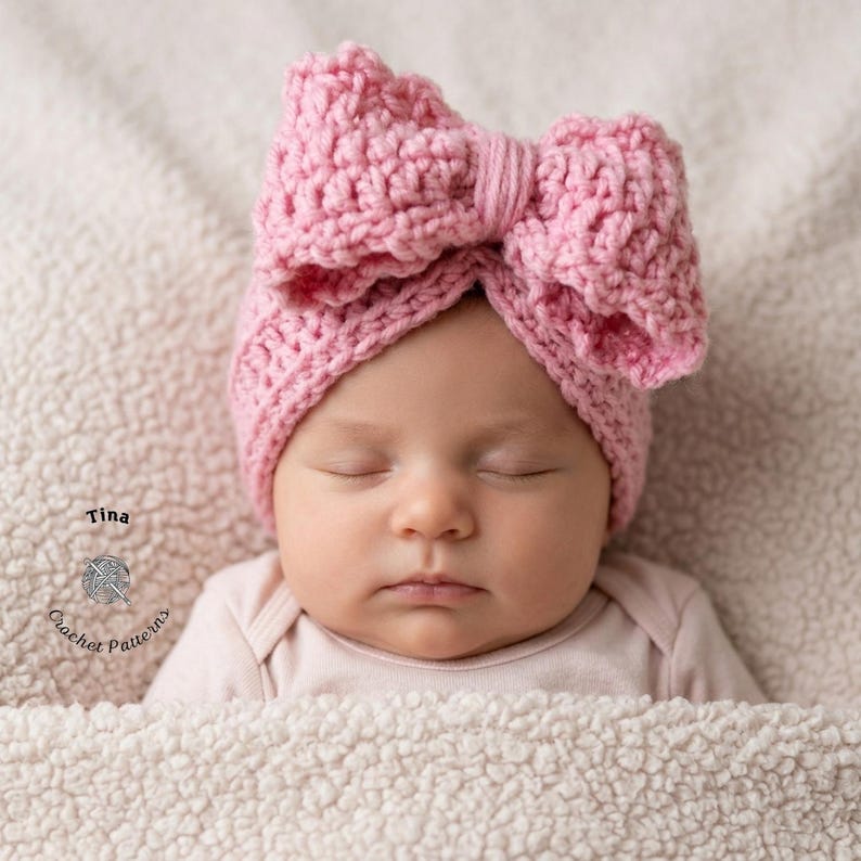 May include: A baby wearing a pink crochet bow headband. The headband is a light pink color and has a large bow on top. The baby is sleeping and is wrapped in a soft, white blanket. The text "Tina Crochet Patterns" is in the lower left corner.