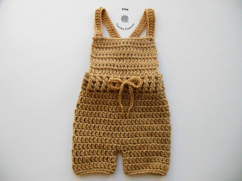Op de afbeelding: Een gehaakte baby romper in een lichtbruine kleur met een strik in de taille. De romper heeft bandjes die in de rug kruisen.