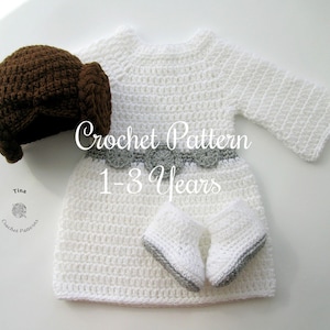 May include: A white crochet baby dress with long sleeves, a gray belt, and matching booties. A brown crochet hat is to the left. The text "Crochet Pattern 1-3 Years" is in the center.
