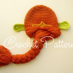 May include: Orange and green crocheted hat with a long braided tail. The hat has two green ear-like flaps and a star-shaped design on the top.