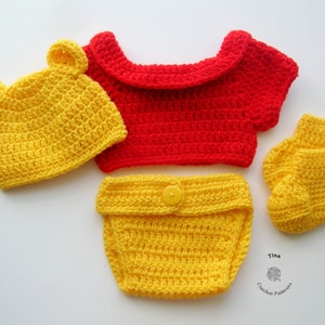 May include: A crocheted baby outfit in yellow and red. The outfit includes a hat with bear ears, a short-sleeved shirt, diaper cover, and booties. The hat, diaper cover, and booties are yellow, and the shirt is red.