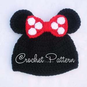May include: A black crochet hat with attached black ears and a red bow with white polka dots. The text "Crochet Pattern" is written on the hat. This handmade hat is suitable for babies and children.