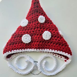 Könnte beinhalten: Ein handgefertigter roter Häkelhut mit weißen Punkten und weißer Bordüre. Der Hut hat eine spitze Spitze und ein weißes, geschlungenes Design um die Gesichtsöffnung. Der Text "Tina Crochet Patterns" ist unten sichtbar.