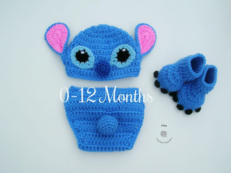 May include: Blue crocheted baby outfit with a Stitch character design. The outfit includes a hat, diaper cover, and booties. The hat has large blue eyes, a pink nose, and pink ears. The diaper cover has a blue tail. The booties have black accents. The outfit is for babies 0-12 months.