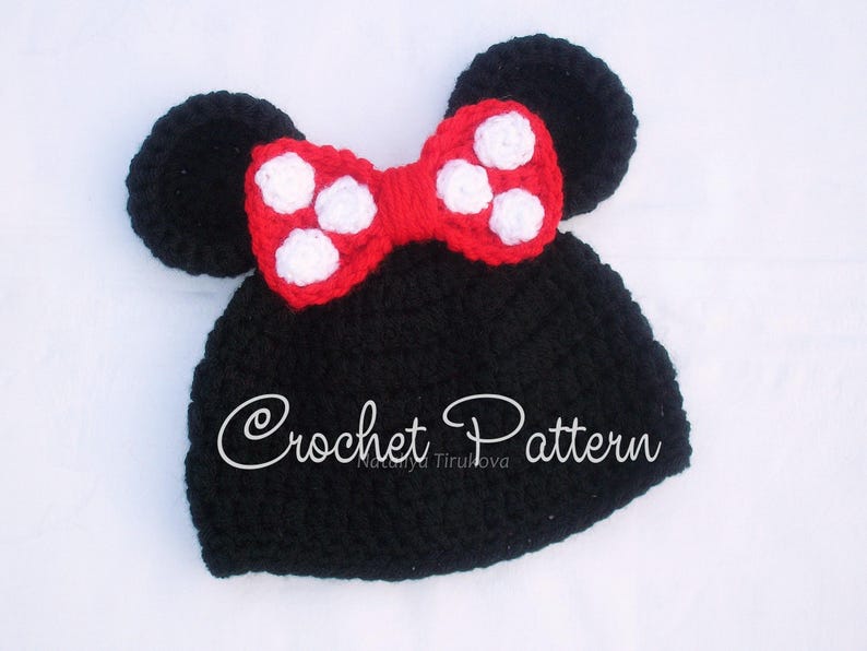May include: A black crochet hat with two round ears and a red bow with white polka dots. The text "Crochet Pattern" is written in cursive on the hat. This handmade hat is a cute accessory.