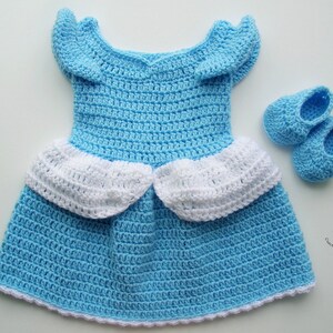 Peut inclure: Une robe de b&eacute;b&eacute; en crochet bleu clair avec des bordures blanches et des chaussures de b&eacute;b&eacute; en crochet bleu clair assorties. La robe a une jupe &agrave; volants et une ouverture dans le dos.