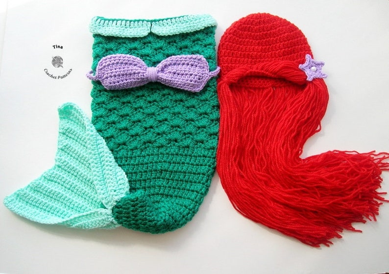 May include: A crocheted mermaid tail costume for a baby, with a green and blue tail, a purple bow, and a matching red crocheted wig with a purple star.