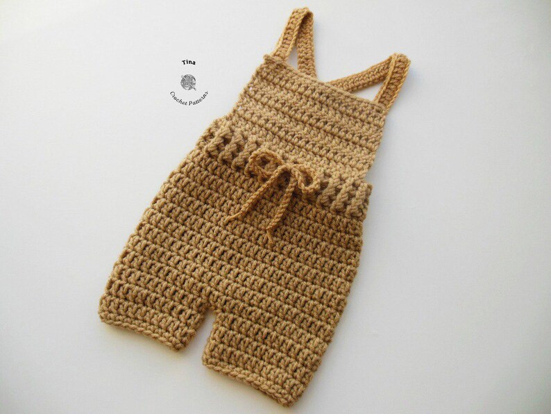 Op de afbeelding: Een gehaakte baby romper in een lichtbruine kleur met verstelbare bandjes en een strik in de taille.