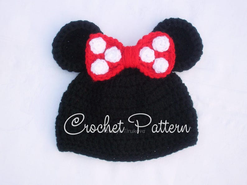 May include: A black crochet hat with attached black ears and a red bow with white polka dots. The text "Crochet Pattern" is written on the hat. This handmade hat is suitable for babies and children.