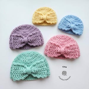 May include: Five crocheted baby hats in pastel colors: yellow, blue, pink, purple, and mint green. Each hat features a bow detail at the front. The hats are arranged on a white surface. The image includes the text "Tina Crochet Patterns".