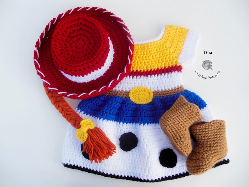 May include: Crocheted baby outfit resembling a cowgirl costume, featuring a red hat with white stitching, a dress with yellow, white, and blue sections, and brown boots. The outfit includes a braided hair piece and a yellow belt buckle.