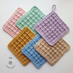 Può includere: Una collezione di sette presine all'uncinetto fatte a mano in vari colori, tra cui rosa, verde, viola, giallo, blu e beige. Ogni presina presenta un motivo a punto waffle strutturato e una forma quadrata. Una presina ha un anello.
