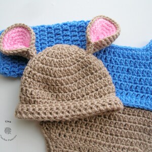 May include: A brown crocheted hat with pink ears and a blue crocheted sweater.