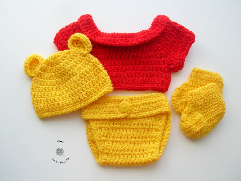 May include: A crocheted baby outfit in yellow and red. The outfit includes a hat, a diaper cover, a shirt, and booties. The hat has bear ears. The shirt has a red collar. The outfit is made with a yellow yarn.