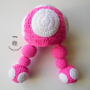 K&ouml;nnte beinhalten: Rosa-wei&szlig;er geh&auml;kelter Pilz mit zwei langen rosa-wei&szlig;en geh&auml;kelten Stielen. Der Pilz hat einen wei&szlig;en Kreis in der Mitte und einen wei&szlig;en Ring um den Kreis. Die Stiele haben einen wei&szlig;en Kreis am Ende.