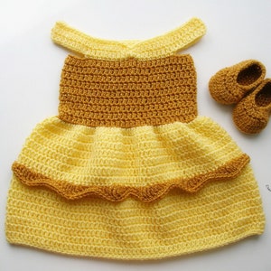 K&ouml;nnte beinhalten: Ein gelbes und braunes H&auml;kelkleid mit einem R&uuml;schen-Saum und passenden H&auml;kelschuhen. Das Kleid hat einen runden Ausschnitt und ist &auml;rmellos. Die Schuhe sind flach und haben eine abgerundete Spitze.