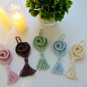 May include: Five crocheted rose-shaped ornaments with tassels in various colors, including pink, brown, green, blue, and cream.