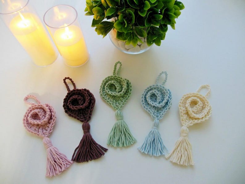 May include: Five crocheted rose-shaped ornaments with tassels in various colors, including pink, brown, green, blue, and cream.