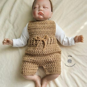 Op de afbeelding: Een beige gebreide baby romper met een strik in de taille. De romper ligt op een wit deken. De tekst "Tina Crochet Patterns" staat in de rechter benedenhoek van de afbeelding.