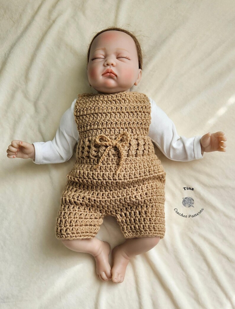 Op de afbeelding: Een beige gebreide baby romper met een strik in de taille. De romper ligt op een wit deken. De tekst "Tina Crochet Patterns" staat in de rechter benedenhoek van de afbeelding.