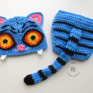 May include: A handmade crochet cat hat and tail set. The hat is blue with pink ears, black accents, and large orange and yellow eyes. The tail is blue with black stripes. A whimsical costume.