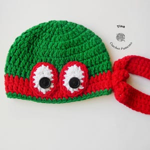 May include: Green crocheted hat with red and white eye appliques and a red crocheted tie. The hat is designed to look like a Teenage Mutant Ninja Turtle.
