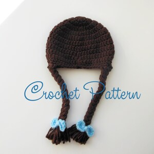 Może przedstawiać: Brązowy kapelusz na szydełku z dwoma długimi brązowymi warkoczami i niebieskimi kokardkami na końcach. "Crochet Pattern" jest napisane niebieskim kolorem pod kapeluszem.
