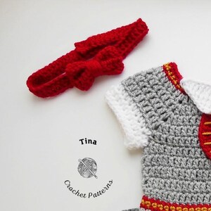 May include: A gray crocheted baby outfit with red and gold accents. The outfit has a white collar and a red bow headband.