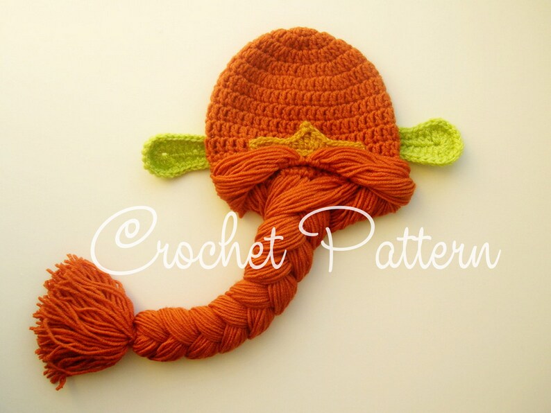 May include: Orange crochet hat with a long braided tail and green leaf-shaped ears. The hat has a yellow star on the top.