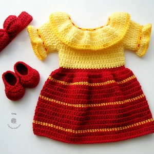 Puede incluir: Un vestido de bebé de ganchillo con un corpiño amarillo y una falda roja con rayas amarillas. El vestido tiene un cuello de volantes amarillo y mangas cortas. El conjunto también incluye una diadema de ganchillo roja y un par de zapatos de ganchillo rojos.