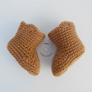 May include: Two handmade, crochet baby booties in a warm, light brown color. The booties are displayed on a white background. The text "Tina Crochet Patterns" is visible in the image.