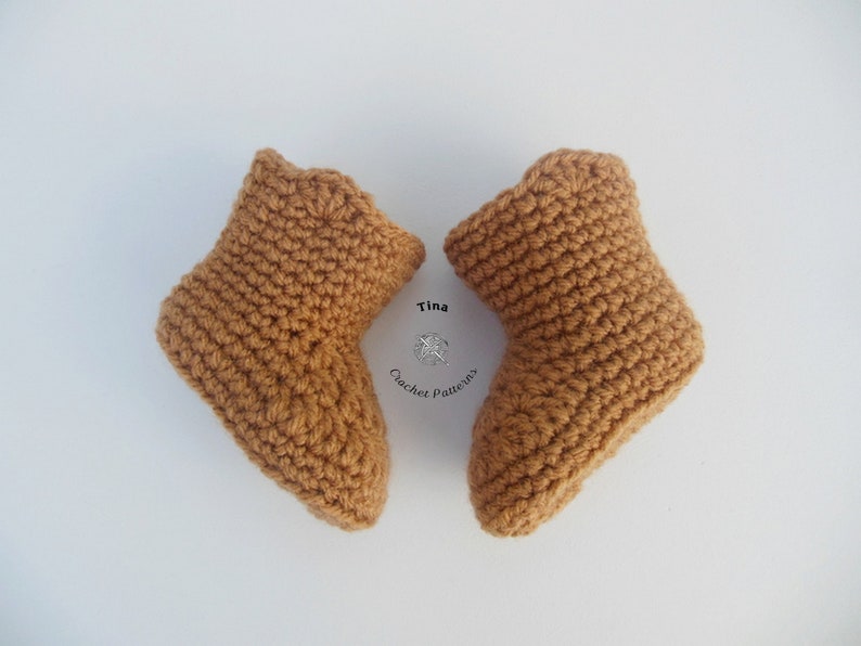 May include: Two handmade, crochet baby booties in a warm, light brown color. The booties are displayed on a white background. The text "Tina Crochet Patterns" is visible in the image.