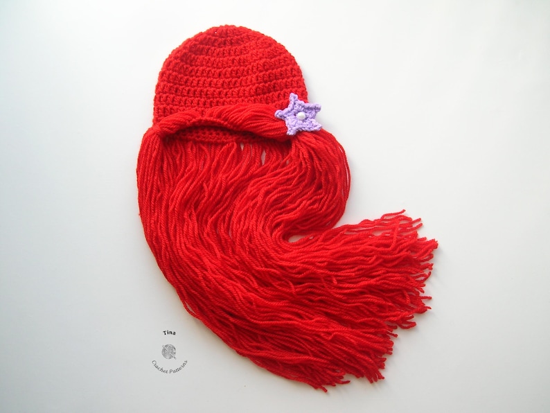May include: Red crocheted hat with a long red yarn tail, resembling hair, and a purple crocheted starfish on top.