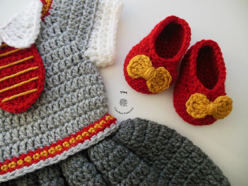 May include: A gray crocheted baby dress with a red and yellow trim, a red crocheted bow, and a red crocheted purse with a yellow stripe. The dress is paired with red crocheted baby shoes with yellow bows.