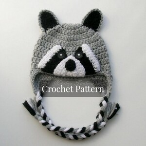 May include: Gray crocheted raccoon hat with black and white details. The hat has a long, braided tail and the text "Crochet Pattern" is printed on the front.
