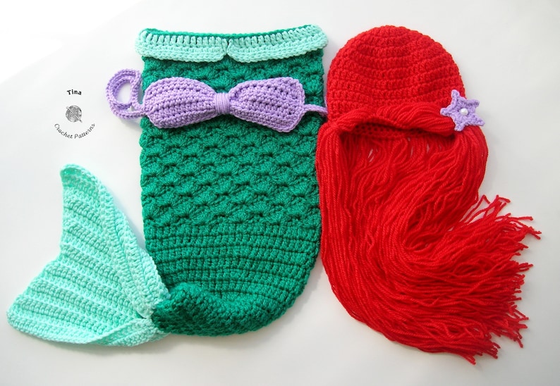 May include: A crocheted mermaid costume for a baby, featuring a green and turquoise tail, a purple bow, and a red crocheted wig with a purple starfish.