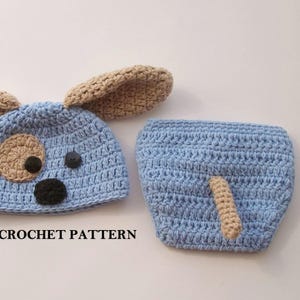 May include: A crochet baby hat and diaper set in blue with brown ears and tail. The hat has a cute dog face with black eyes and nose and a brown button for the mouth. The diaper has a brown tail.