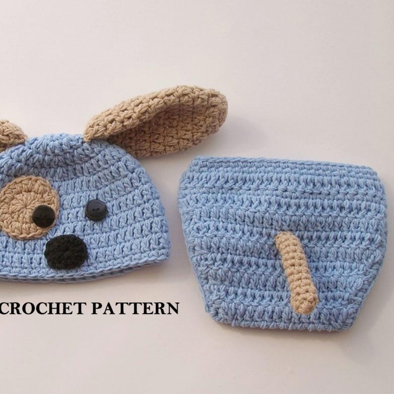 May include: A crochet baby hat and diaper set in blue with brown ears and tail. The hat has a cute dog face with black eyes and nose and a brown button for the mouth. The diaper has a brown tail.