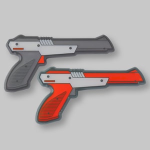 May include: Two toy guns, one gray and one red, with a white stripe and black details. The guns are in a side-by-side view.
