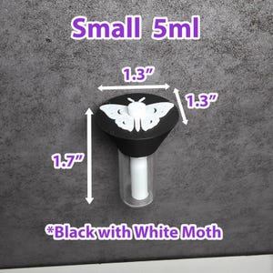 May include: A small, clear glass bottle with a black cap featuring a white moth design. The bottle is 4.3 cm tall, and the cap is 3.3 cm in diameter. The text "Small 5ml" and "Black with White Moth" are also visible.
