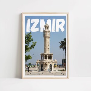 May include: A white poster with the word "IZMIR" in large, white, block letters with a distressed texture. The poster features a photo of a clock tower in Izmir, Turkey. The clock tower is a white stone structure with a tall, slender tower and a domed roof. The tower is surrounded by a small plaza with trees and people.
