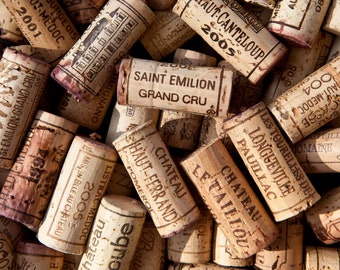 May include: A close-up of a pile of wine corks with various French wine labels, including Saint Emilion Grand Cru, Haut-Ferrand Pomerol, and Les Tourelles de Longueville Pauillac.