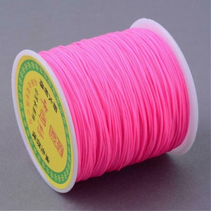 May include: A spool of bright pink elastic cord, wound around a white plastic spool with a yellow label that has Chinese characters printed on it.