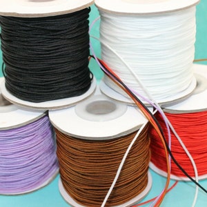 May include: A selection of colourful cord spools in black, white, red, brown, and lavender. The cords are tightly wound on cardboard spools. The image is taken from a slightly elevated angle, showcasing the variety of colours.