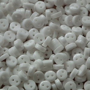 May include: A large pile of white plastic buttons with two holes each. The buttons are small and round.