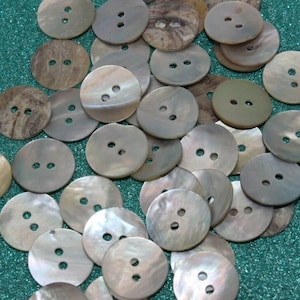 May include: A collection of round, iridescent, mother-of-pearl buttons with two holes each. The buttons are scattered on a green, sparkly surface.