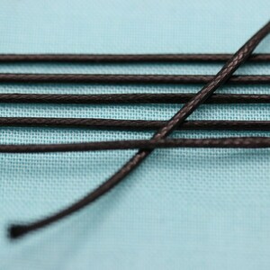 May include: Close-up of black waxed cord on a light blue surface. The cord is arranged in a criss-cross pattern.