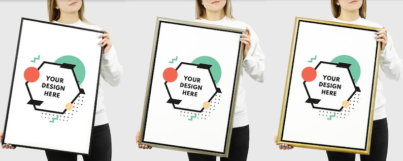 May include: Three people are holding up blank poster frames with black, silver, and gold frames. The posters have a geometric design with a hexagon shape that says "Your Design Here" in black text. The background is a light grey.