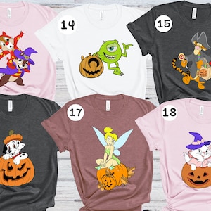 Op de afbeelding: Zes verschillende T-shirts met verschillende Disney-figuren in Halloween-kostuums. De shirts zijn roze, wit, grijs en bruin. De figuren zijn Chip en Chap,  Sulley van Monsters Inc.,  Tinkerbell en een kat.
